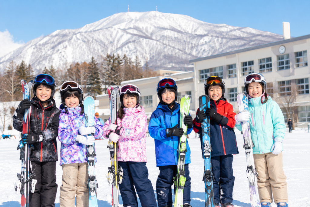 札幌の小学校のスキー授業で、スキー板、ブーツ、ウェアを一式装備して雪山に並ぶ子どもたち